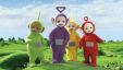 Green, purple, yellow and red plush characters standing in the middle of a green field and a blue sky in the background.